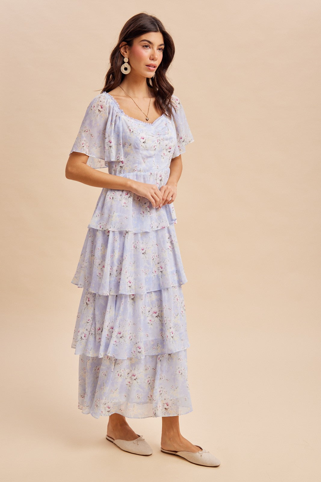 woman wearing a light blue floral tiered maxi dress with flutter sleeves and a fitted bodice