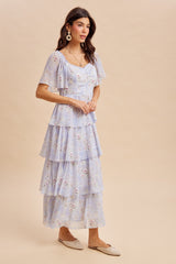 woman wearing a light blue floral tiered maxi dress with flutter sleeves and a fitted bodice