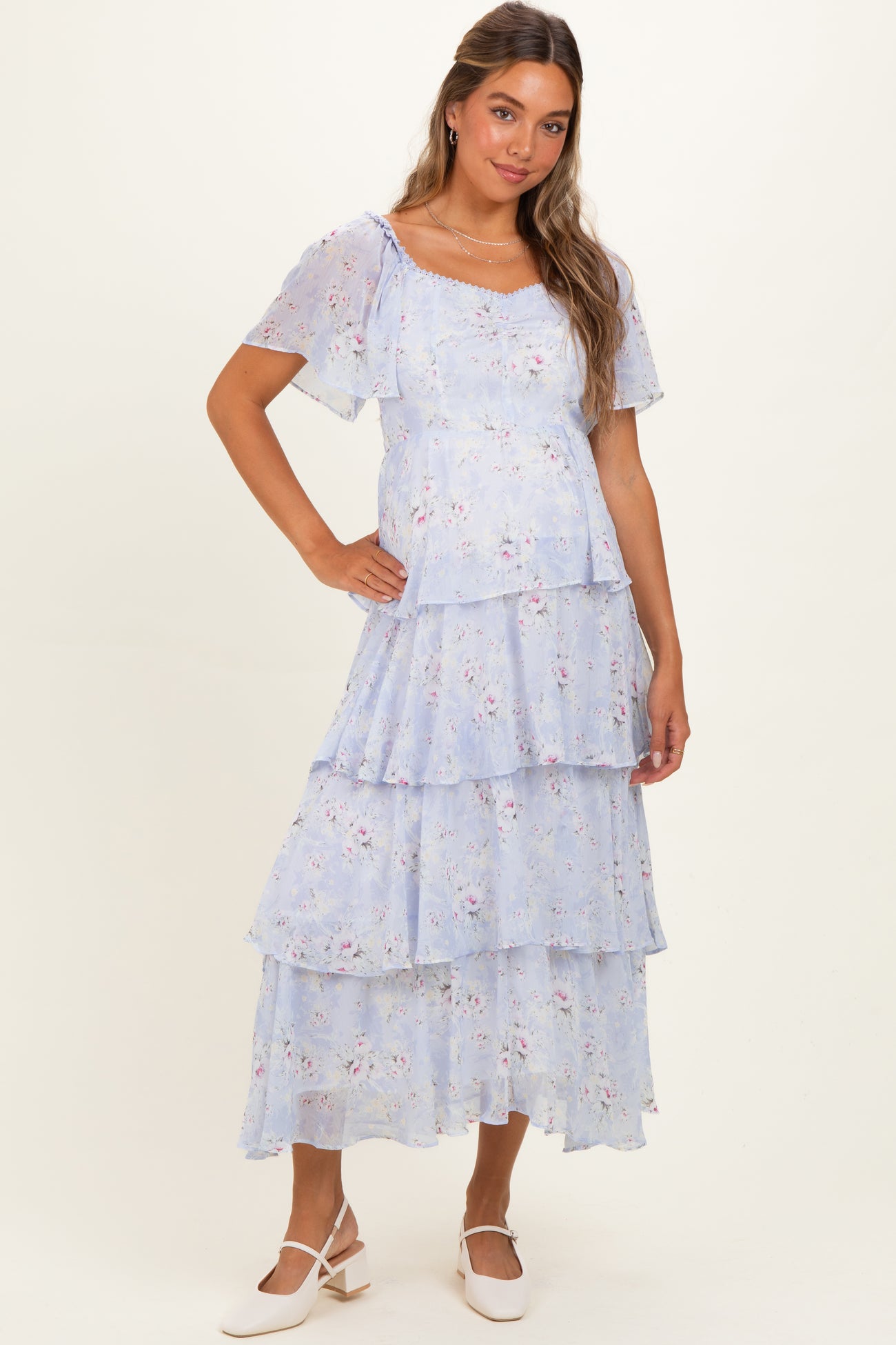 woman wearing a light blue floral maternity dress with tiered layers and short sleeves, showcasing her baby bump