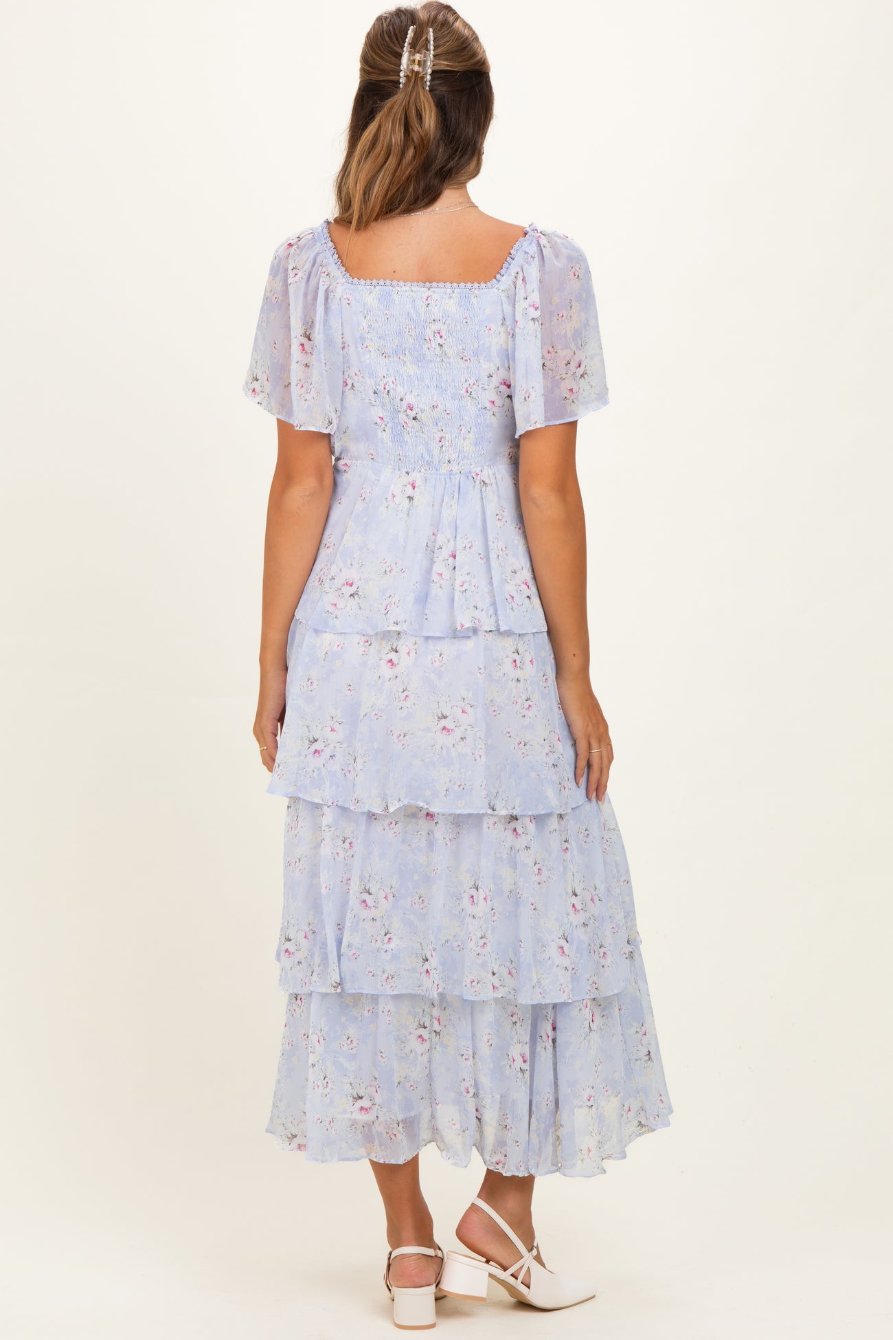 woman wearing a light blue floral maternity dress with tiered ruffles and short sleeves, showing a baby bump from the back