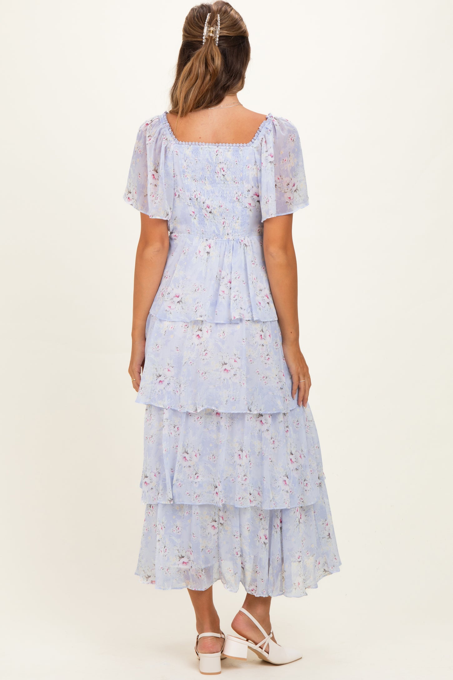 woman wearing a light blue floral maternity dress with tiered ruffles and short sleeves, showing a baby bump from the back