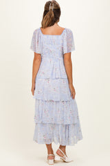 woman wearing a light blue floral maternity dress with tiered ruffles and short sleeves, showing a baby bump from the back
