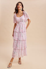 woman wearing a light pink maxi dress with tiered ruffles and floral print, standing against a neutral background