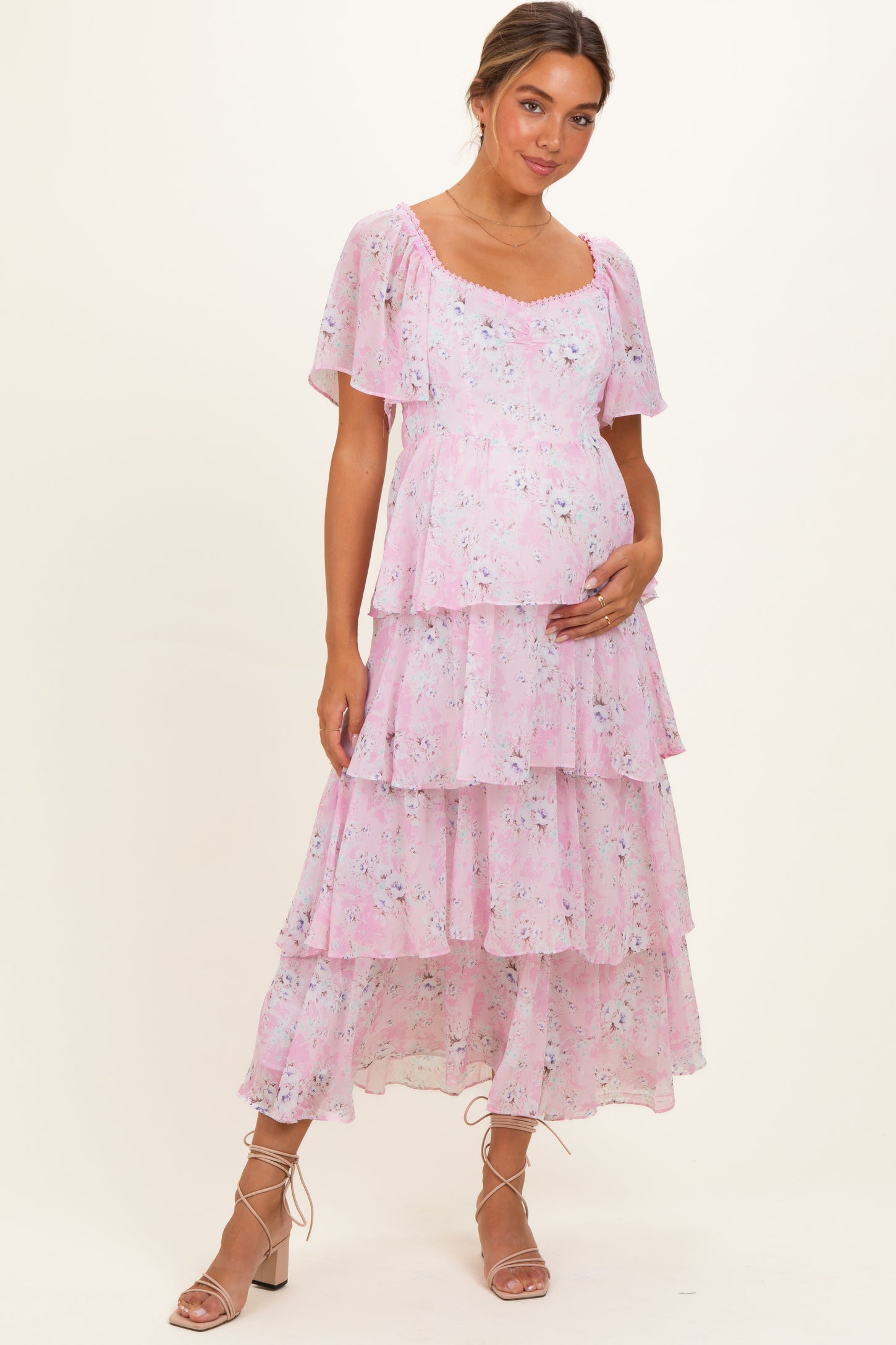 woman wearing a pink floral maternity dress with flutter sleeves and tiered ruffles, holding her baby bump