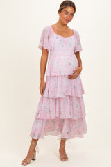 woman wearing a pink floral maternity dress with flutter sleeves and tiered ruffles, holding her baby bump