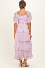 woman wearing a pink floral maternity dress with tiered ruffles and short puff sleeves, viewed from the back