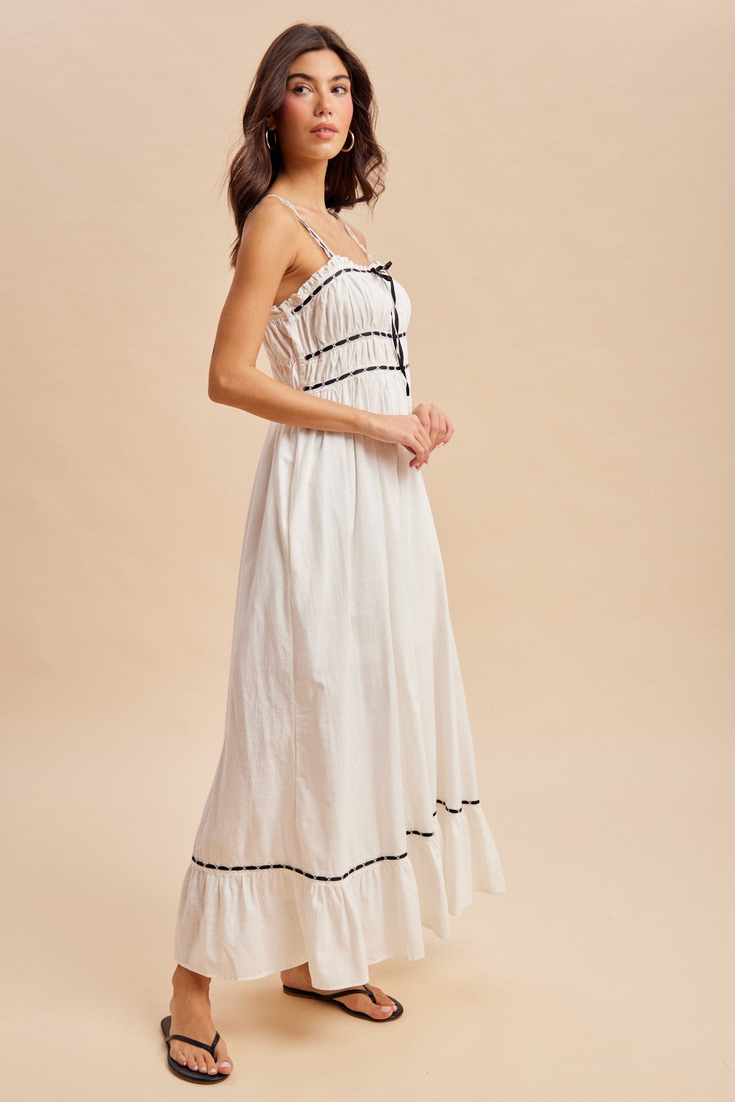woman wearing a white maxi dress with black trim and a gathered bodice, standing against a neutral background