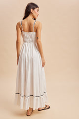 woman wearing a white maxi dress with smocked back and black detailing, viewed from the back