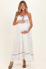 woman wearing a white maternity maxi dress with black trim and a baby bump, smiling and holding her belly