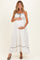 woman wearing a white maternity maxi dress with black trim and a baby bump, smiling and holding her belly