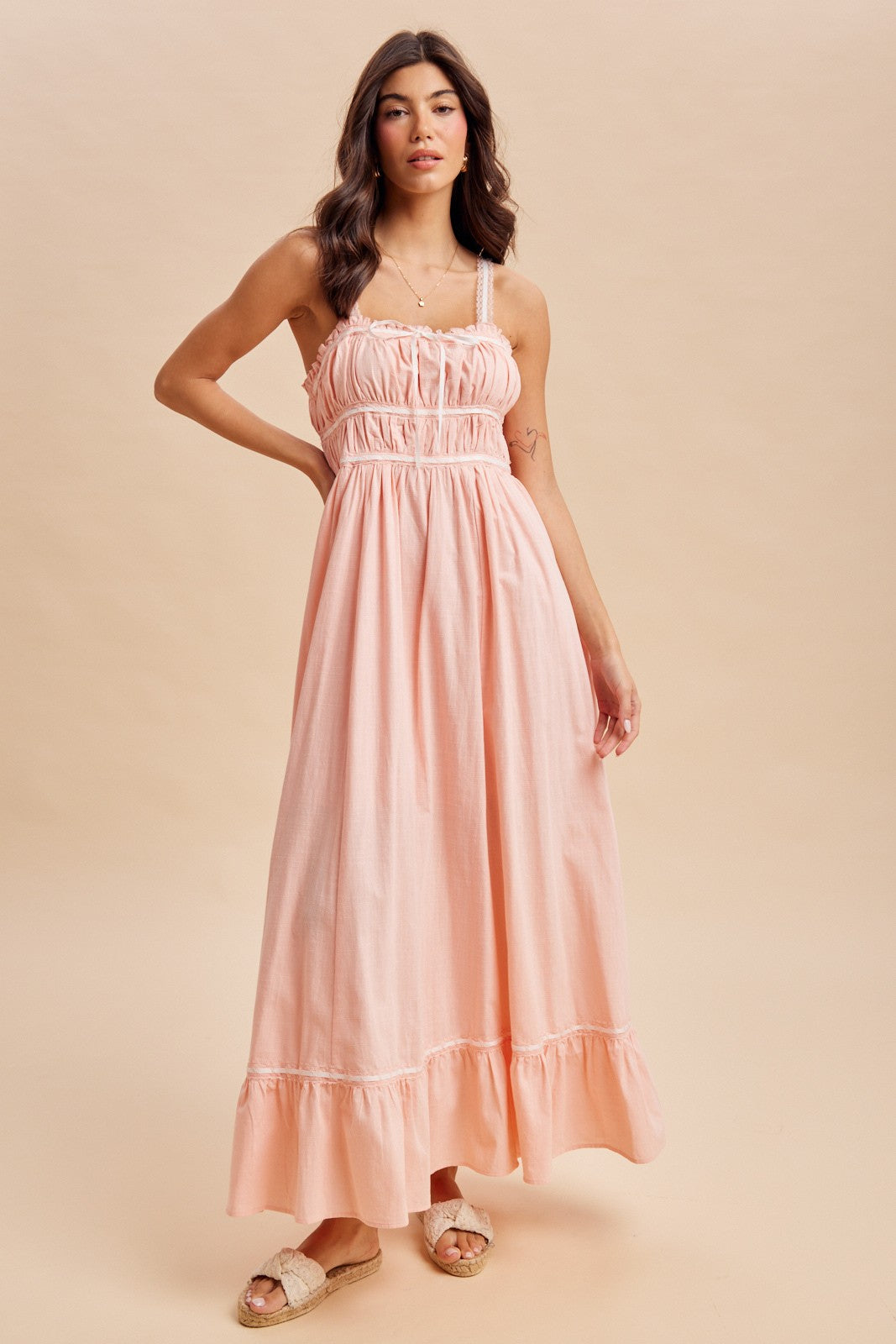woman wearing a light pink maxi dress with adjustable straps and a tiered ruffle hem