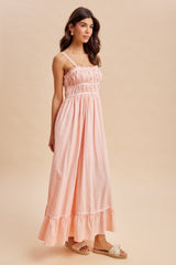 woman wearing a light pink maxi dress with spaghetti straps and ruffle hem details