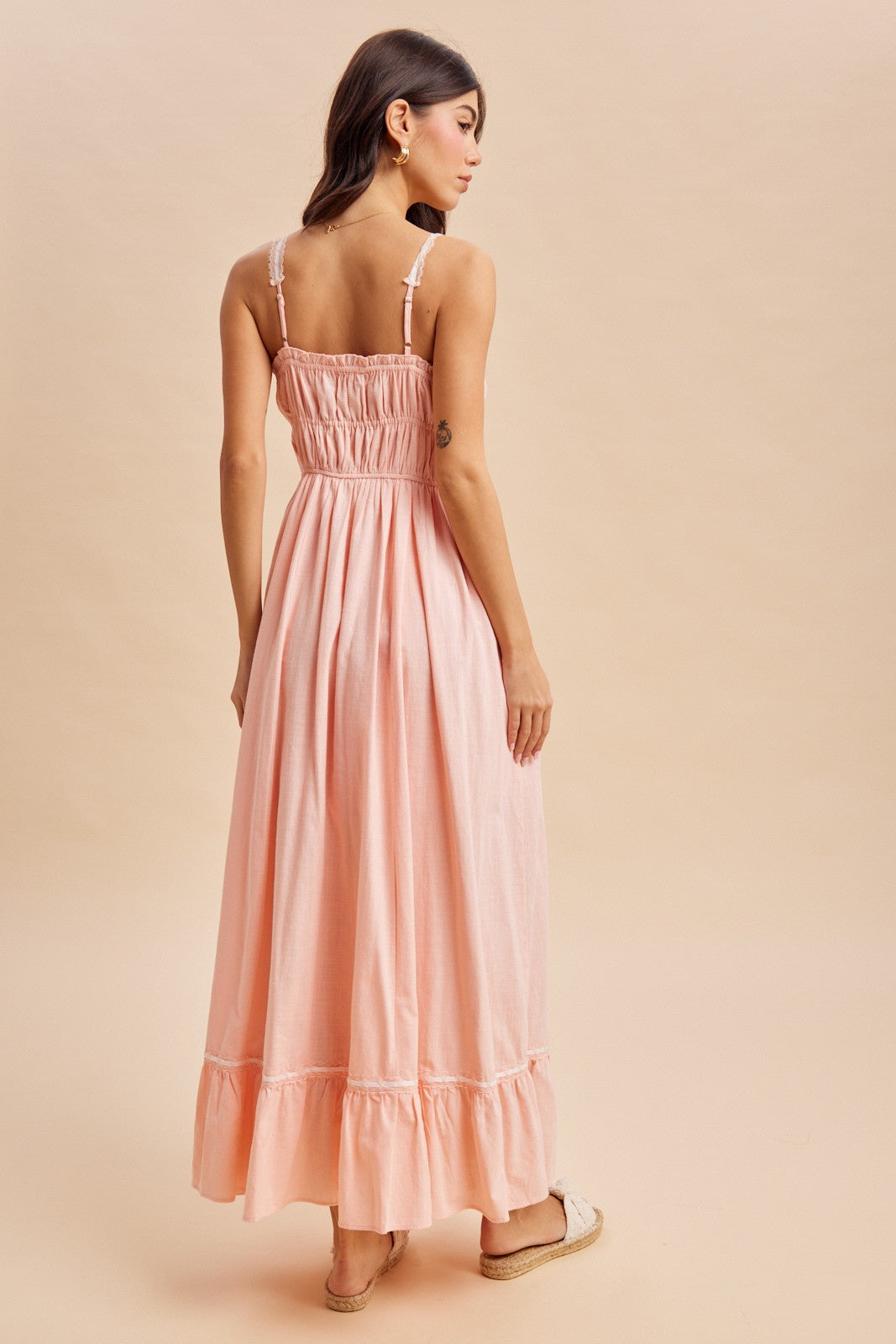 woman wearing a pink maxi dress with a smocked back and ruffled hem, standing against a neutral background
