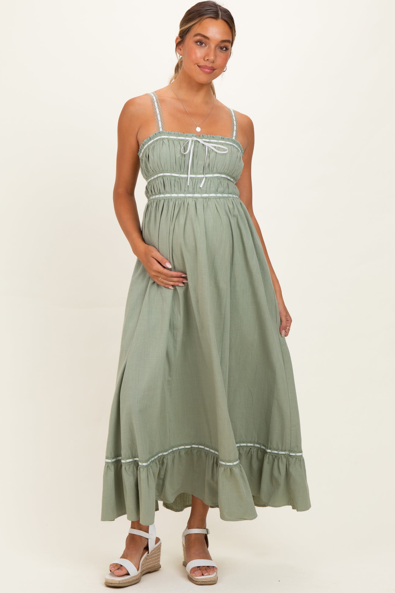 woman wearing a sage green maternity dress with a gathered bodice and ruffled hem, holding her baby bump