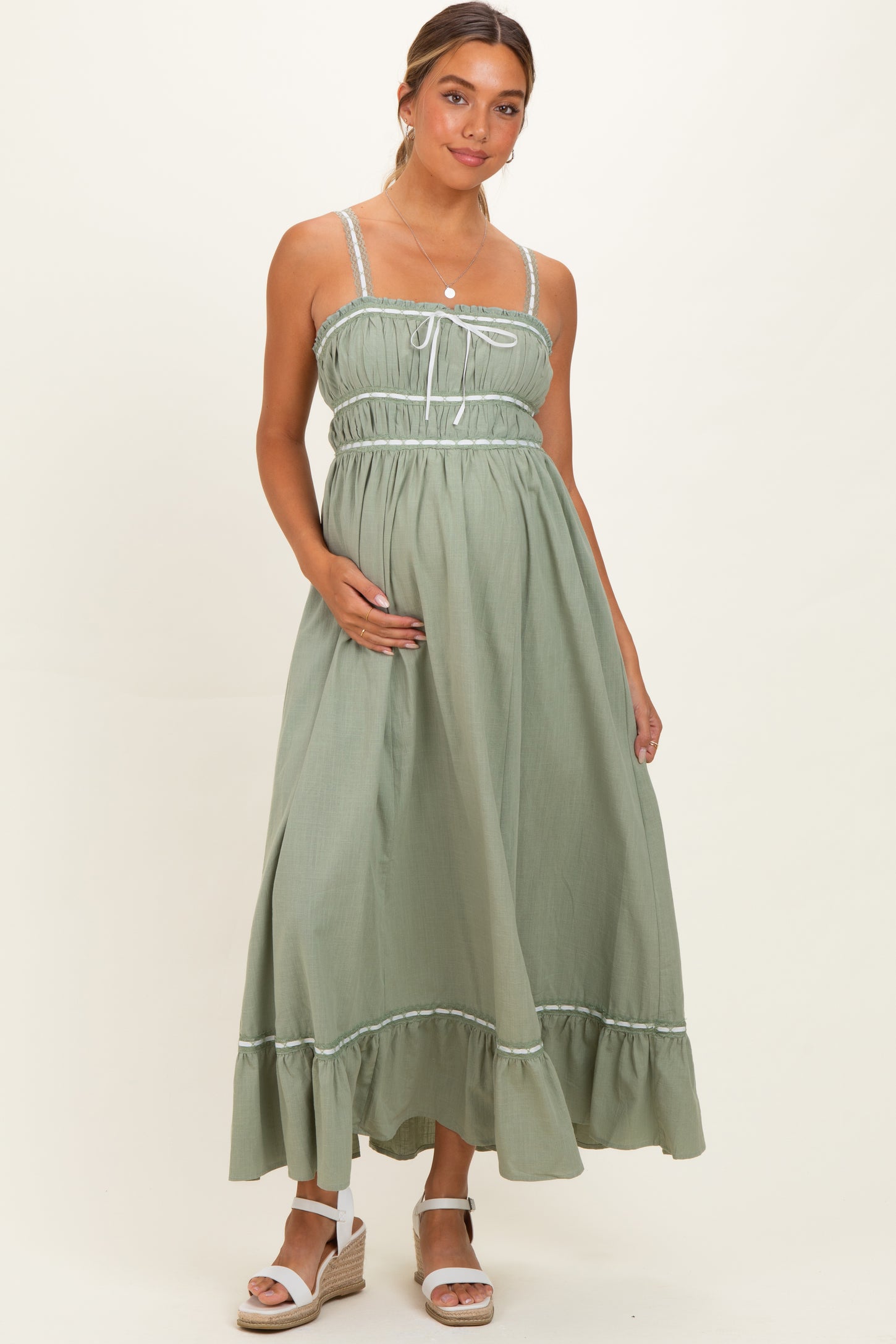 woman wearing a sage green maternity dress with a gathered bodice and ruffled hem, holding her baby bump