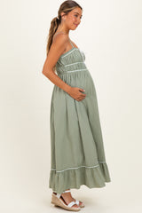 woman wearing a sage green maternity maxi dress with adjustable straps and ruffle hem, cradling her baby bump
