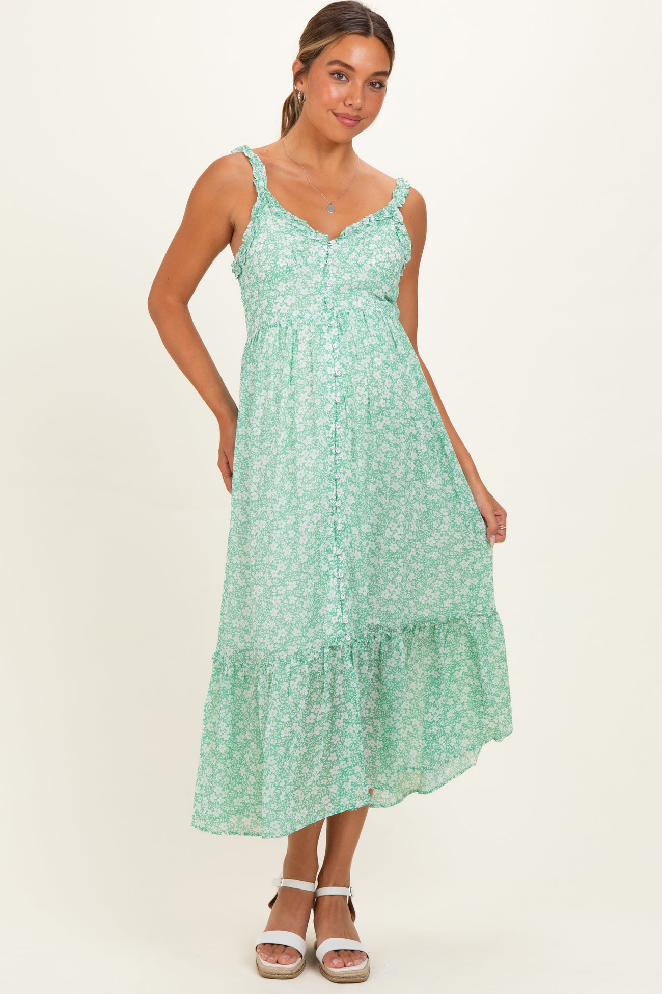 woman wearing a green floral print maternity dress with ruffled hem and button details, showcasing her baby bump