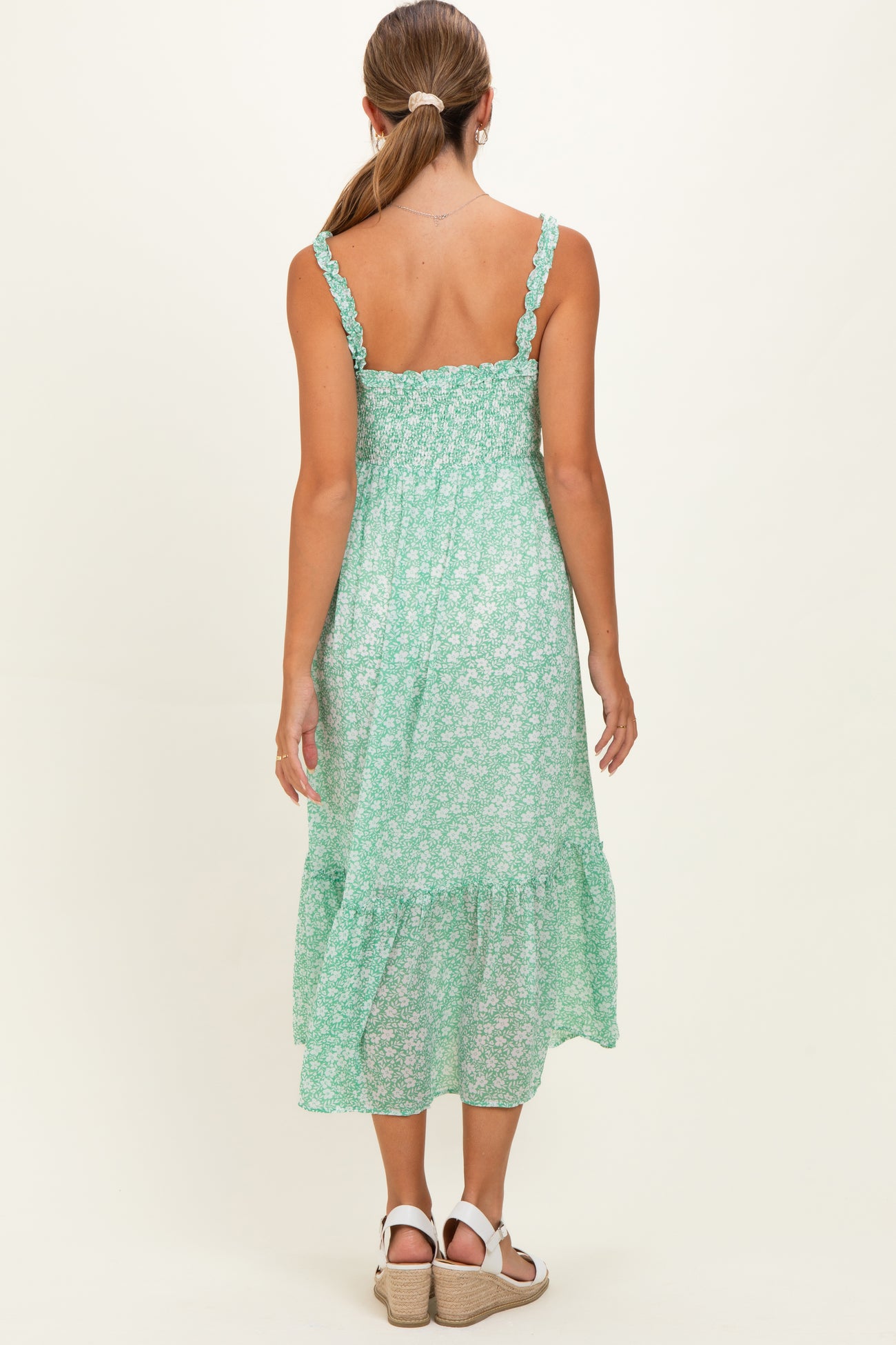woman wearing a green floral print maternity dress with elastic smocking and tiered skirt, view from the back