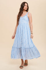 woman wearing a light blue floral maxi dress with buttons and ruffled hem, standing against a neutral background