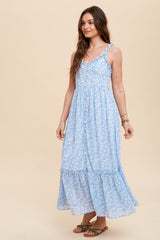 woman wearing a light blue floral maxi dress with button details and a tiered hem, standing against a neutral background