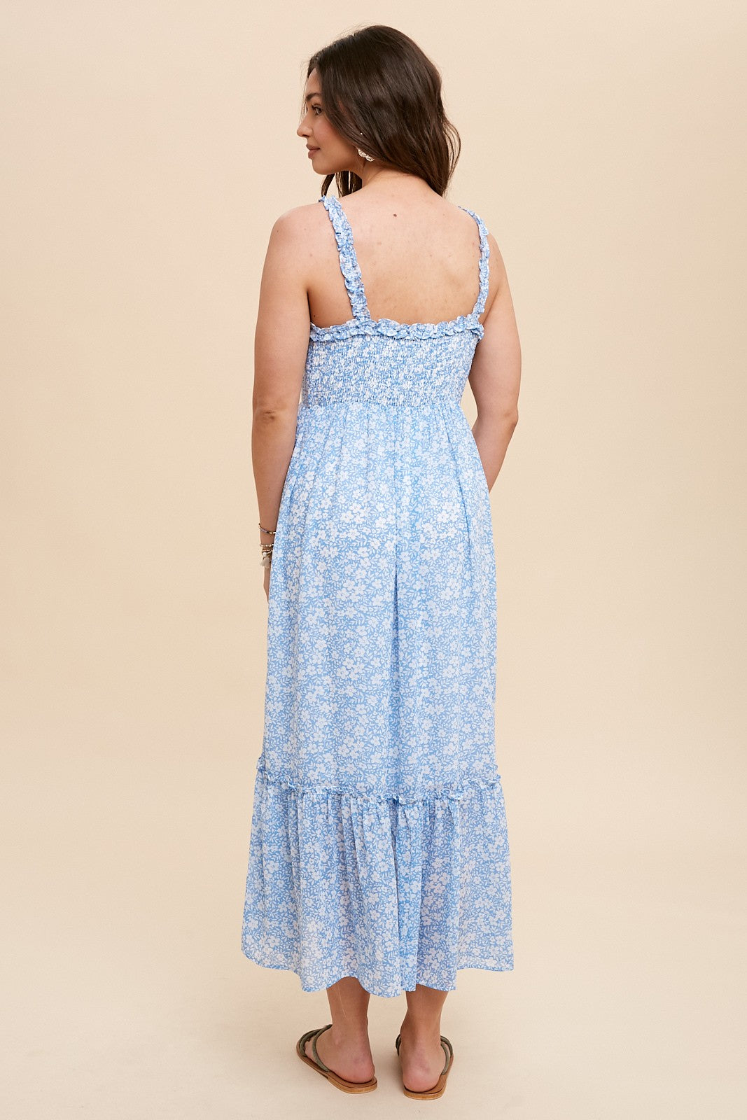 woman wearing a light blue floral maxi dress with ruffle hem and adjustable straps, standing against a beige background