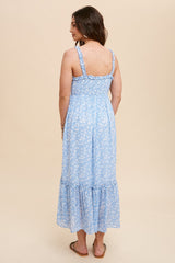 woman wearing a light blue floral maxi dress with ruffle hem and adjustable straps, standing against a beige background