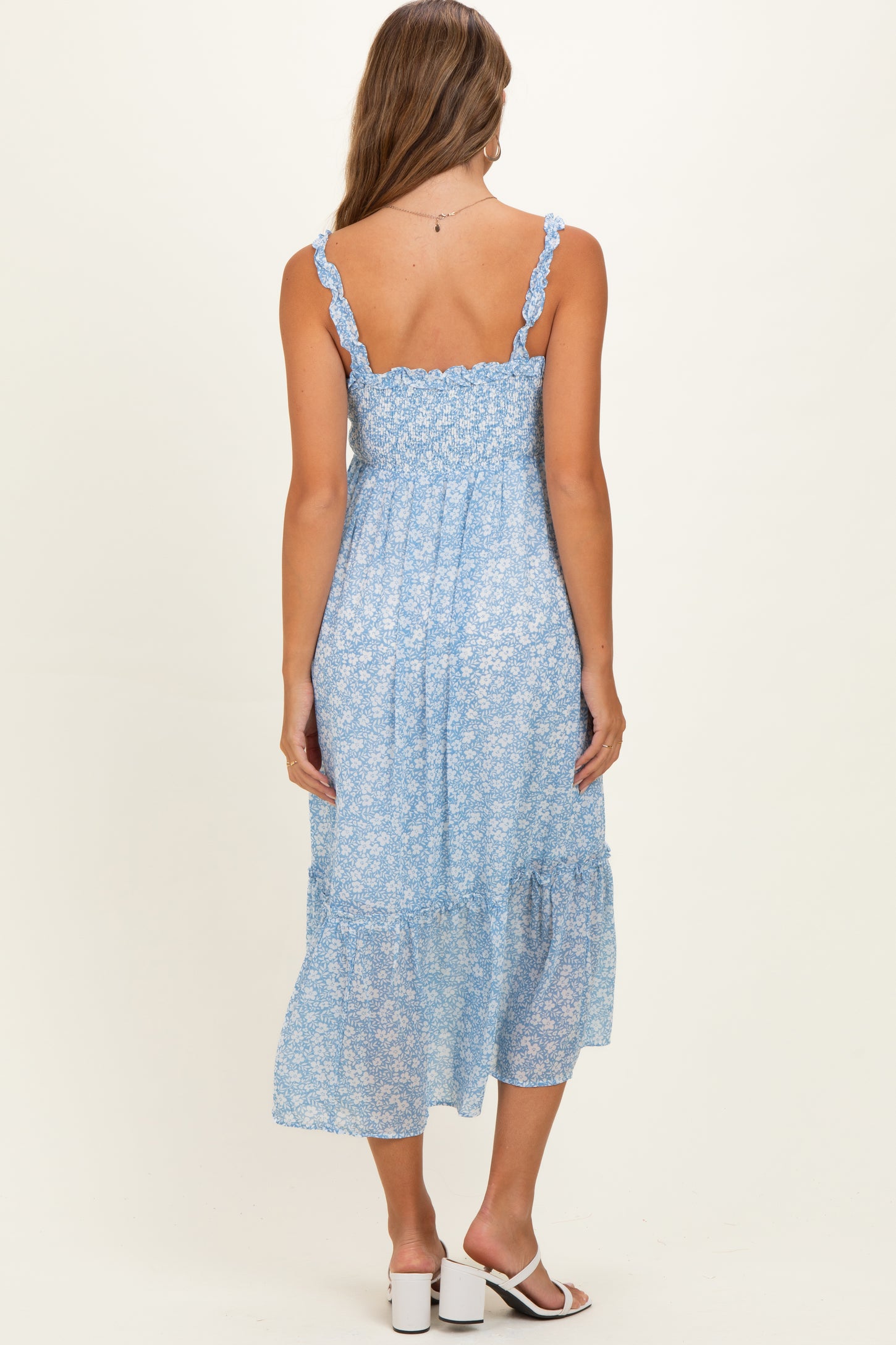 woman wearing a light blue floral maternity dress with adjustable straps and a tiered skirt, showing a baby bump
