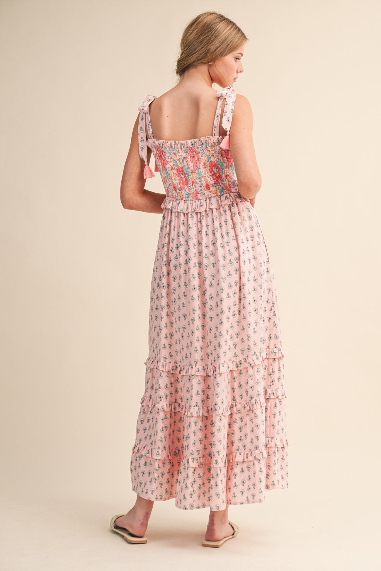 woman wearing a pink floral maxi dress with smocked bodice and ruffled tiers, showing back detail and tie straps