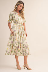 woman wearing a cream floral midi dress with ruffles and a tie waist, paired with yellow strappy heels