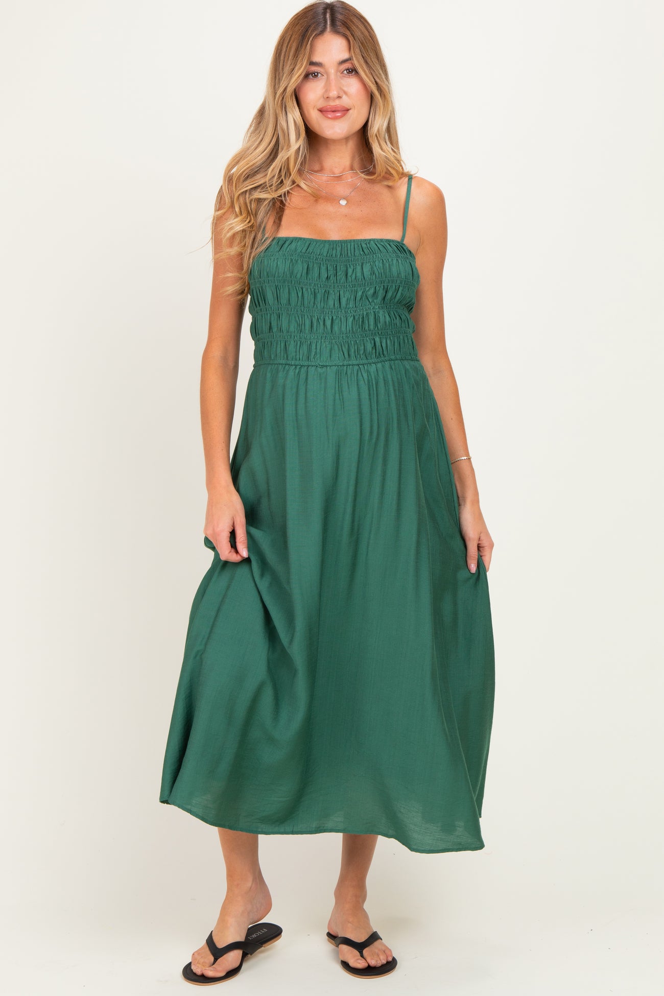 woman wearing a green maternity dress with smocked bodice and spaghetti straps, standing in a relaxed pose