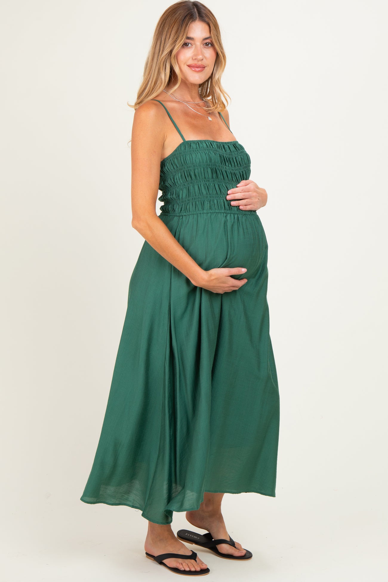 woman wearing a green maternity maxi dress with a smocked bodice and holding her baby bump