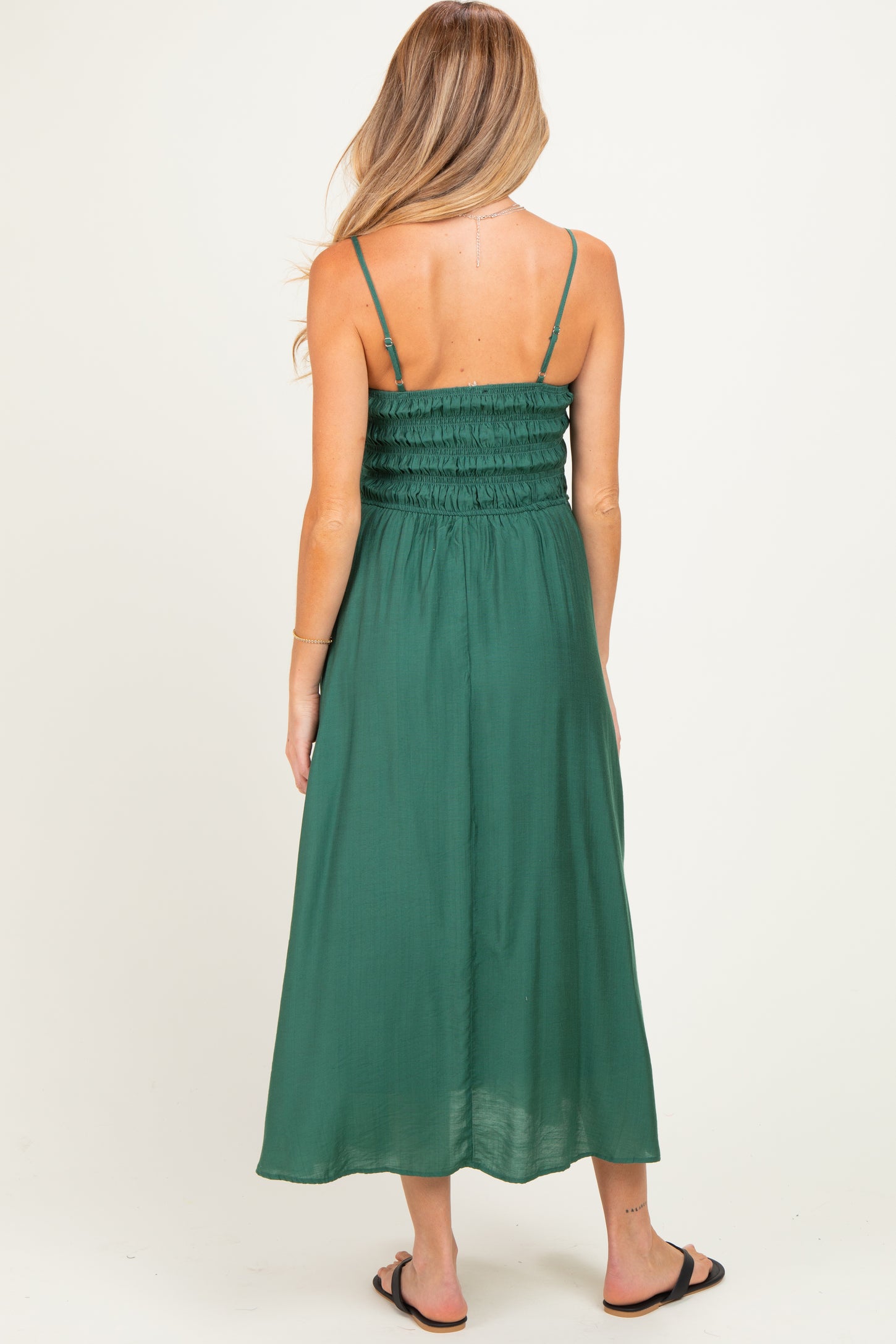 woman wearing a dark green maternity maxi dress with smocked bodice and adjustable straps, viewed from the back