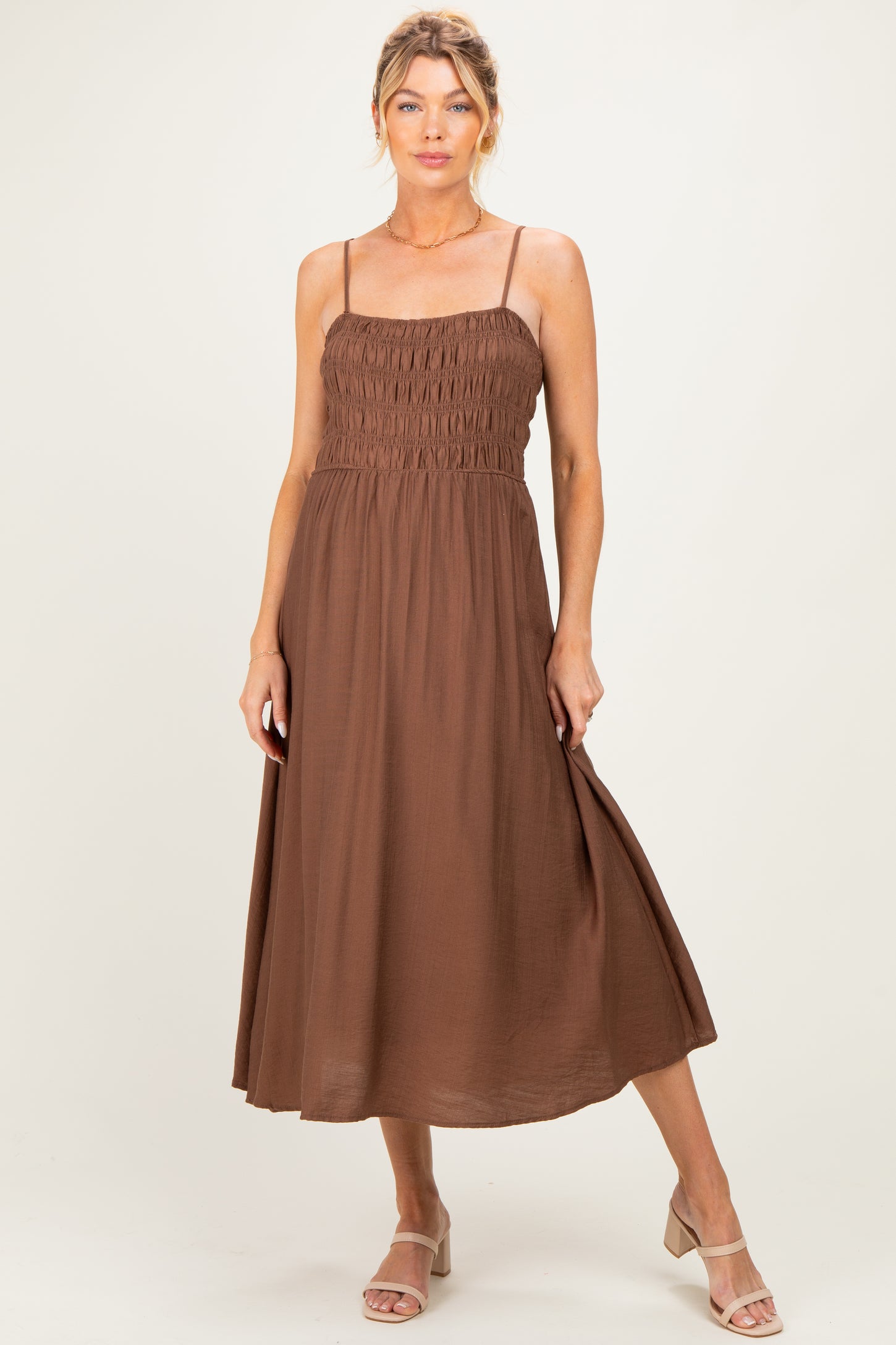woman wearing a brown smocked maternity dress with adjustable straps and a flowing skirt