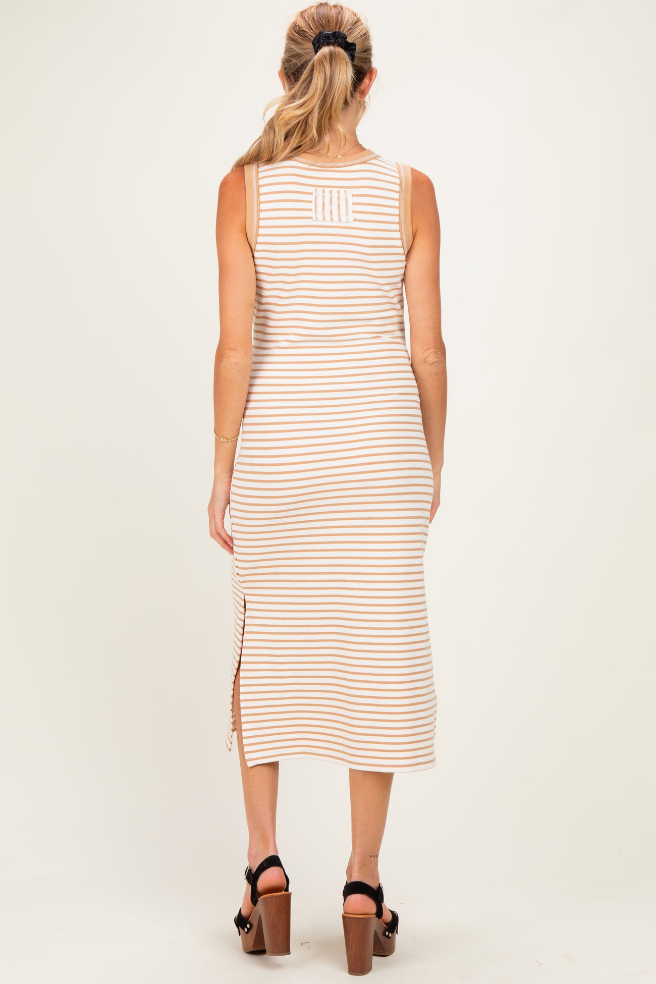 woman wearing a striped beige maternity dress with side slit and a fitted silhouette, shown from the back
