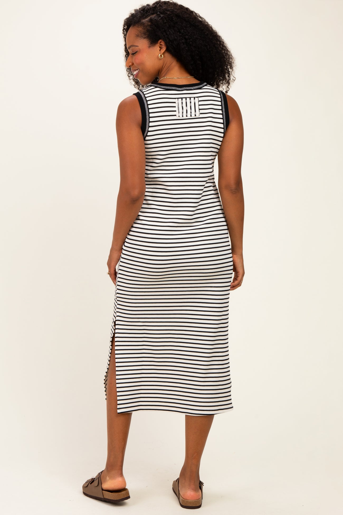 woman wearing a black and white striped sleeveless midi dress with side slits and a round neckline, facing away from the camera