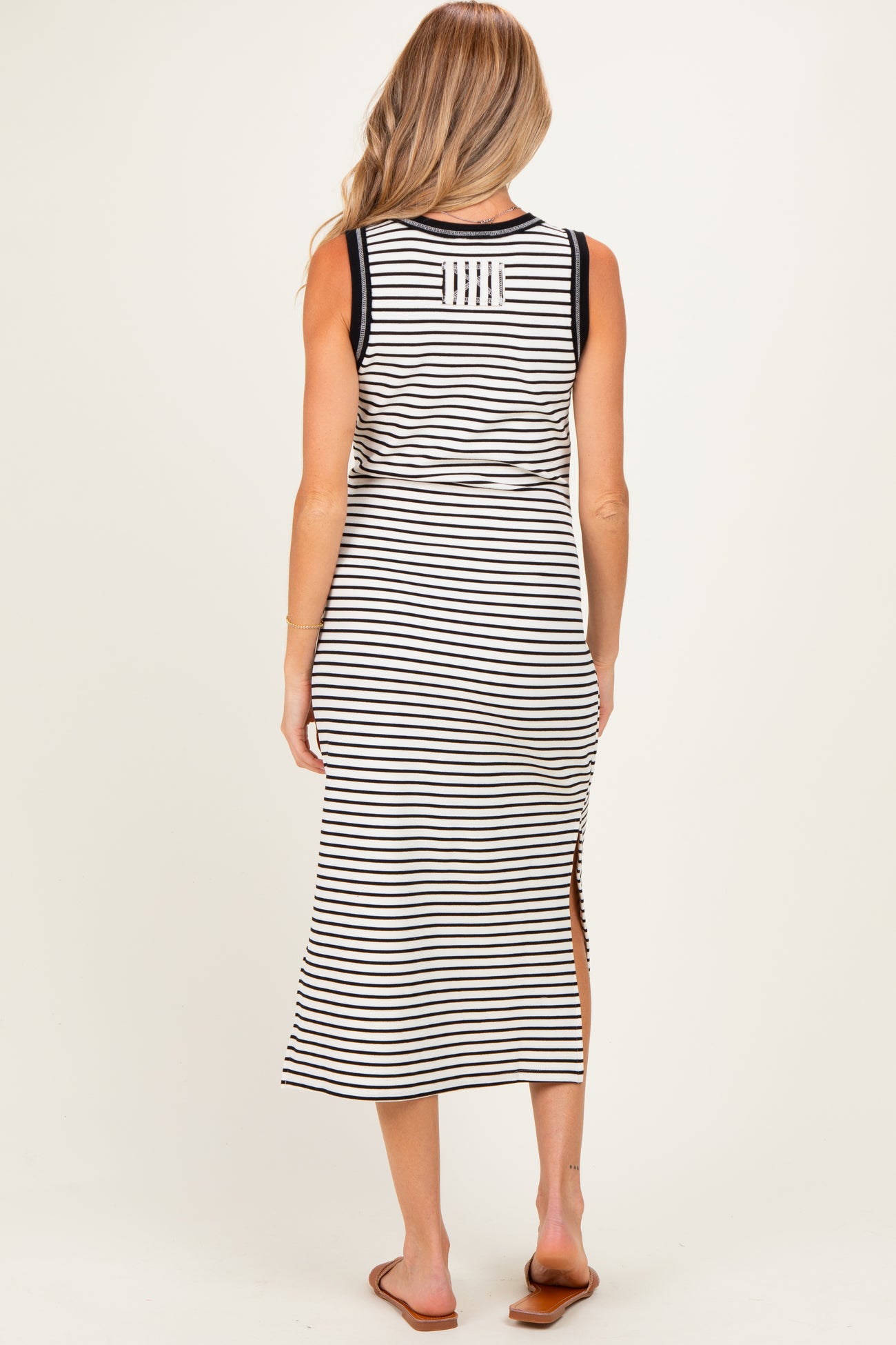 woman wearing a striped maternity maxi dress with side slits and a sleeveless design, showing her pregnant belly