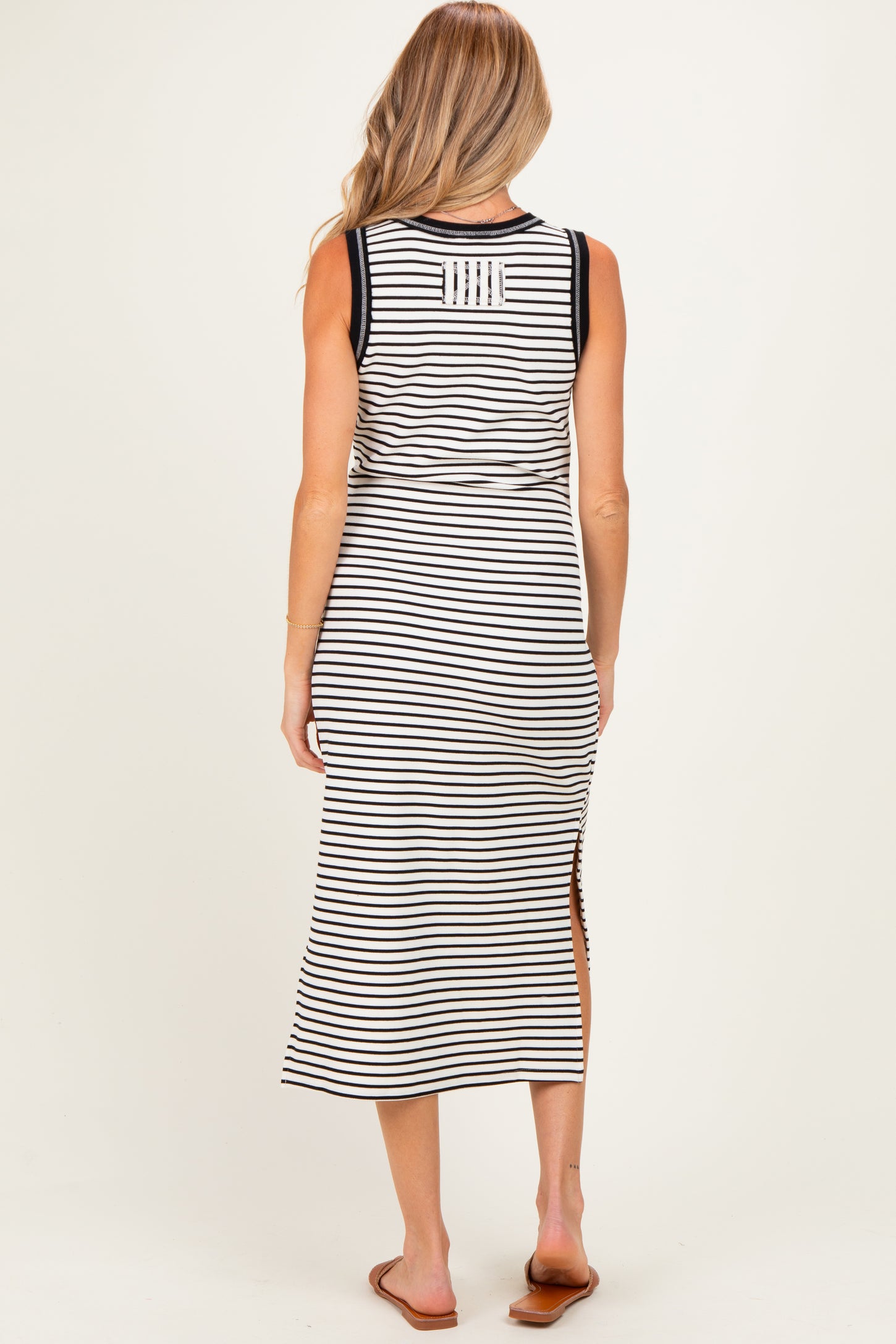 woman wearing a striped maternity maxi dress with side slits and a sleeveless design, showing her pregnant belly
