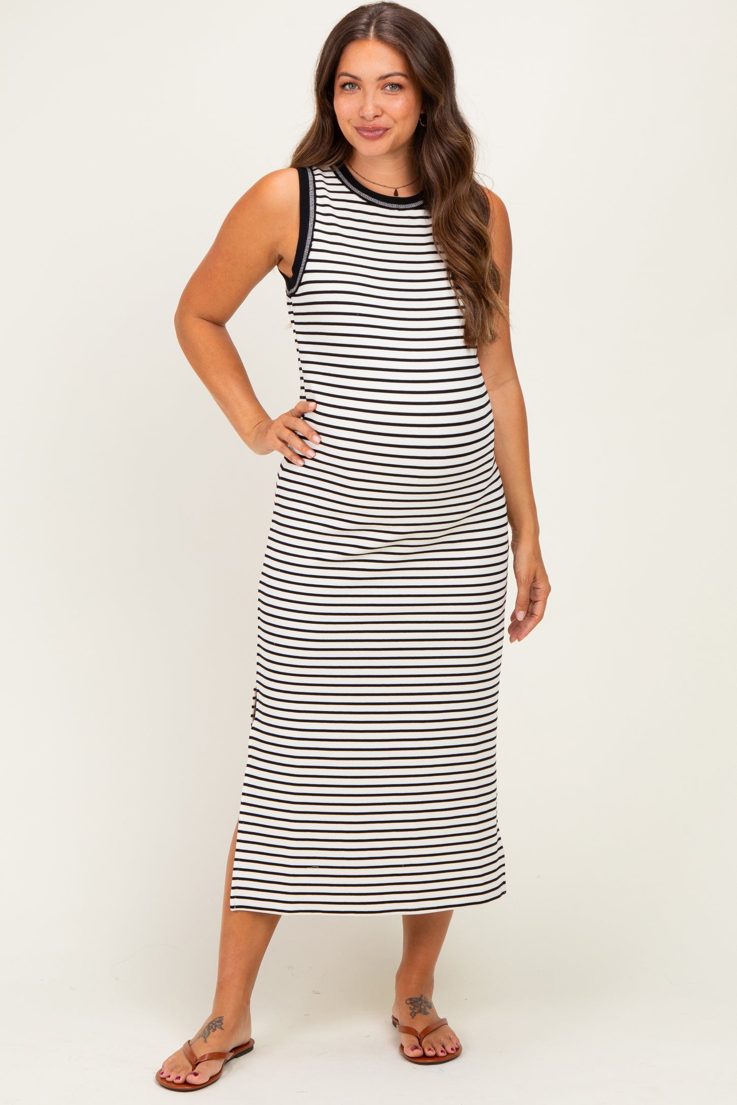 woman wearing a black and white striped maternity maxi dress with a fitted style and side slits, showing her baby bump