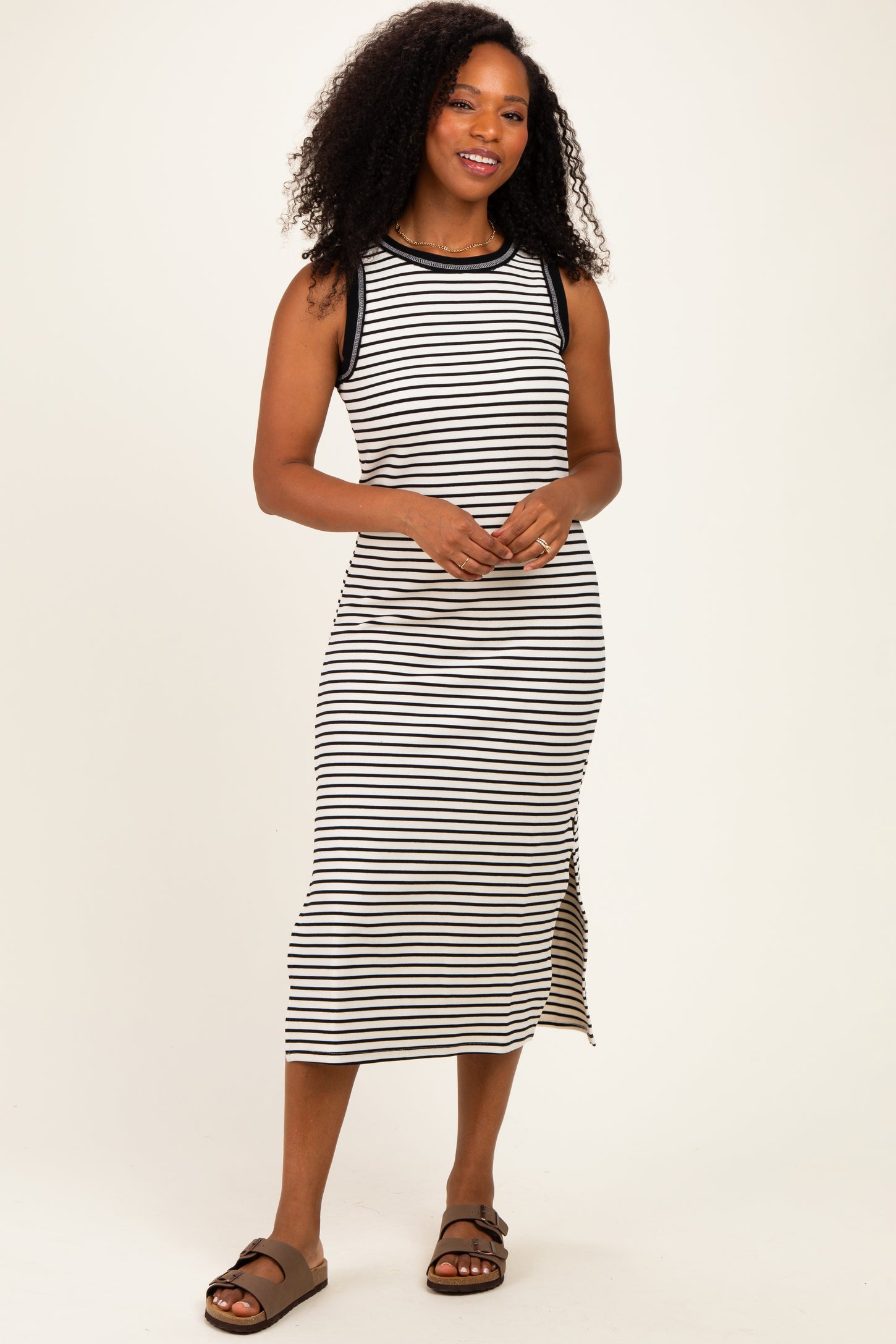 woman wearing a black and white striped sleeveless midi dress with side slit and brown slide sandals
