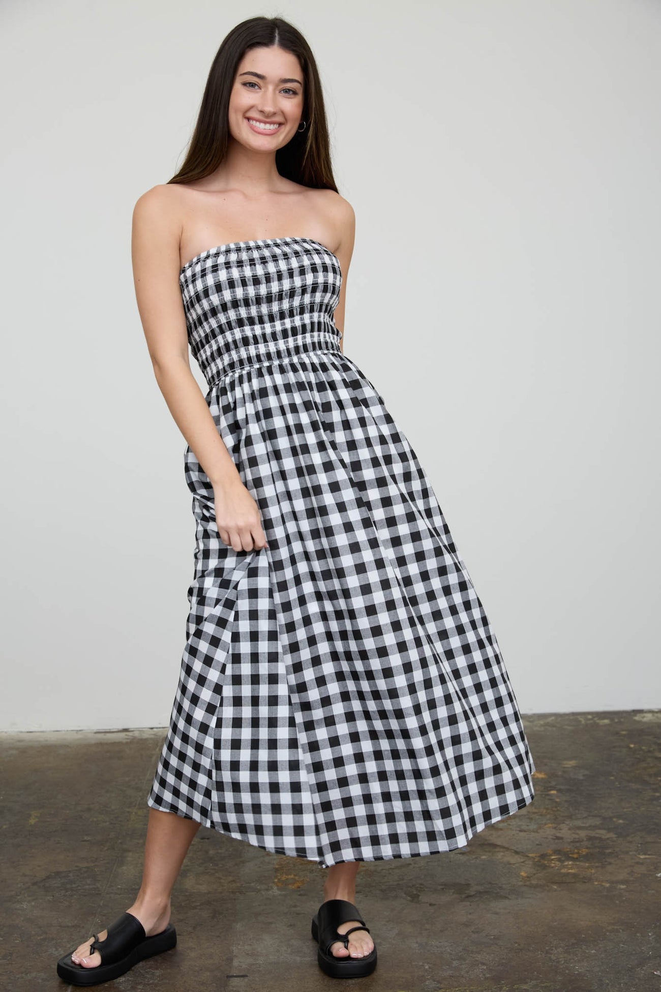 woman wearing a black and white gingham strapless maxi dress and black slide sandals
