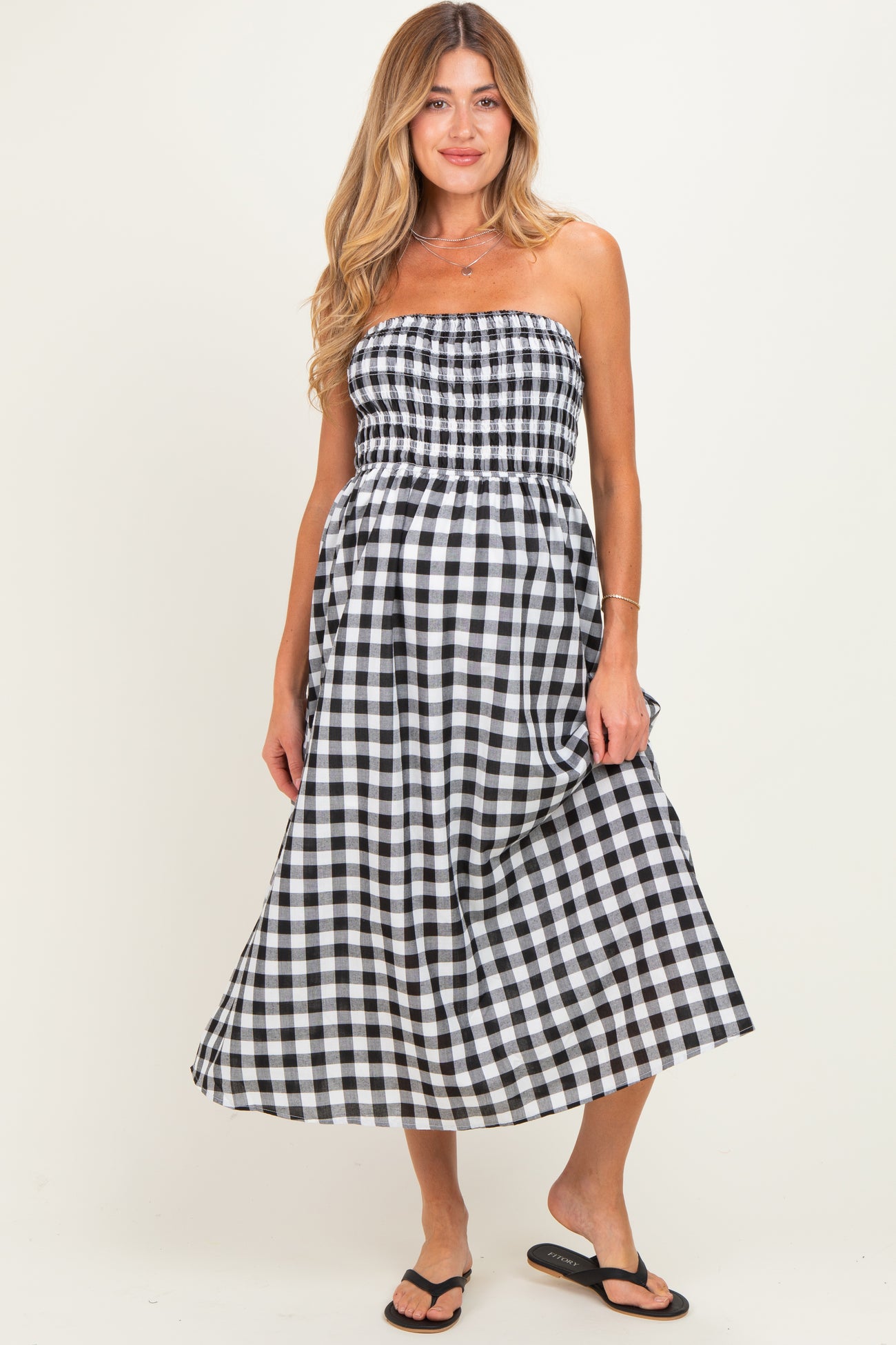 woman wearing a black and white gingham strapless maternity dress with a smocked bodice and flowing skirt, baby bump visible