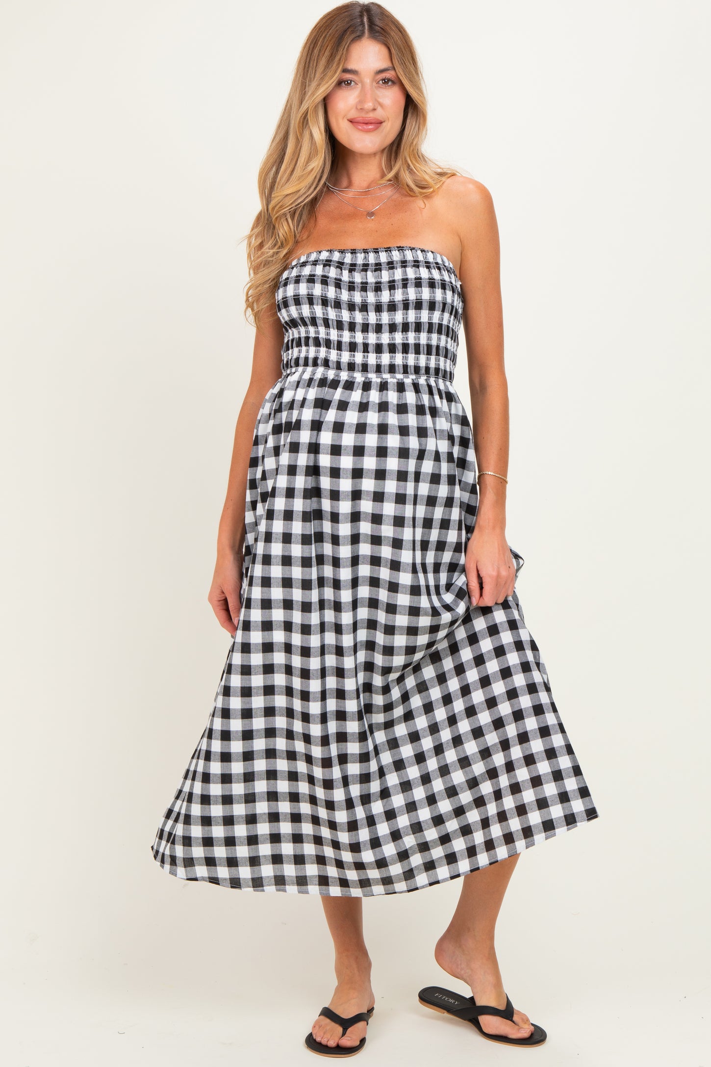 woman wearing a black and white gingham strapless maternity dress with a smocked bodice and flowing skirt, baby bump visible