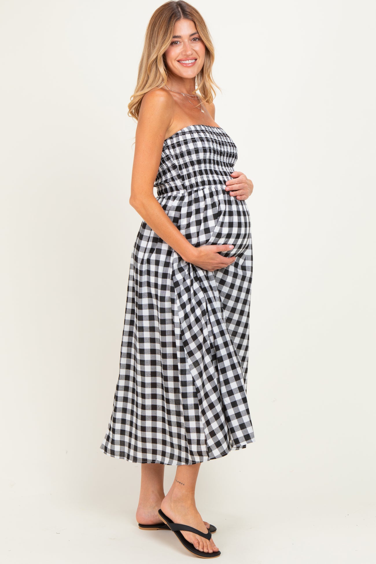 woman wearing a black and white gingham strapless maternity dress and holding her baby bump