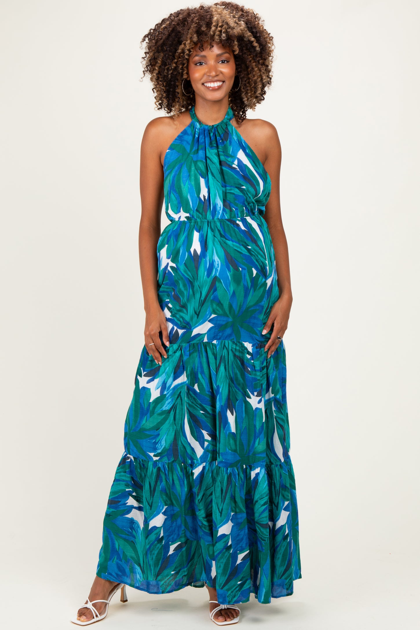 woman wearing a blue tropical print maternity maxi dress with a halter neck and tiered skirt, revealing her baby bump