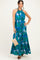 woman wearing a tropical print halter neck maxi dress in shades of blue and green, holding a straw bag