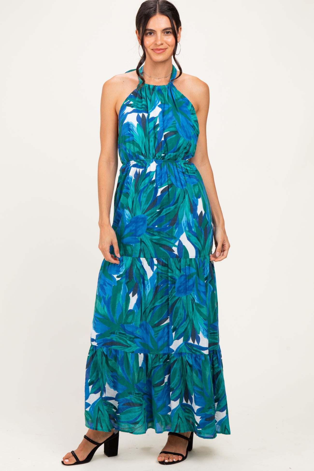 woman wearing a green and blue floral halter neck maxi dress with a tiered skirt and black strappy heels