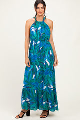 woman wearing a green and blue floral halter neck maxi dress with a tiered skirt and black strappy heels