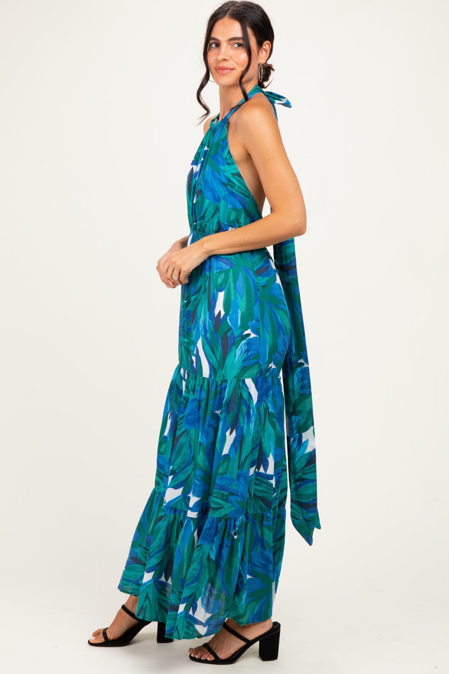 woman wearing a green tropical print maxi dress with a halter neck and cascading ruffles, styled with black sandals