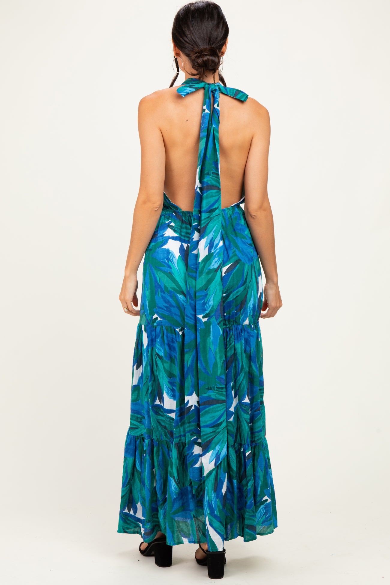woman wearing a backless maxi dress with a green and blue tropical print and a halter tie at the neck