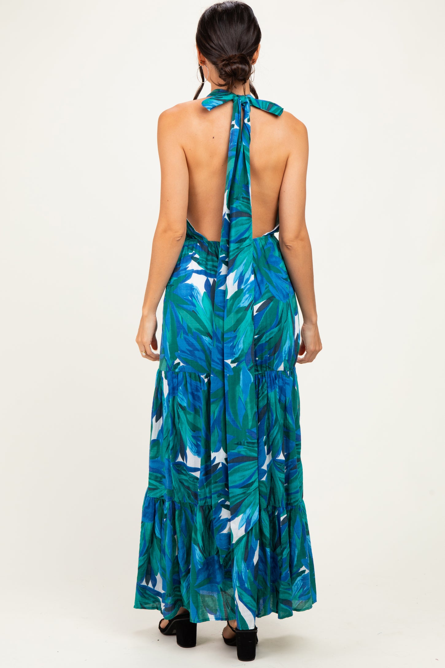 woman wearing a backless maxi dress with a green and blue tropical print and a halter tie at the neck